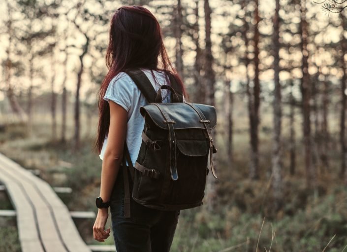 Back view of a tourist girl with backpack walk on a wooden footpath in a beautiful forest.
